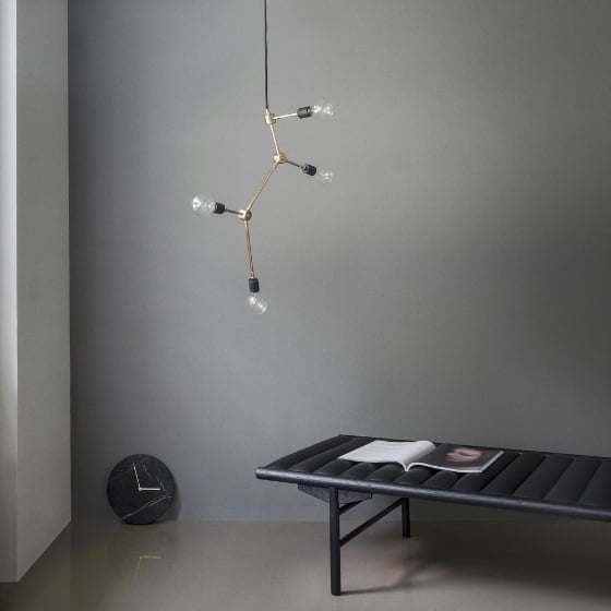 Black marble clock on floor against grey wall with brass light fitting and black bench