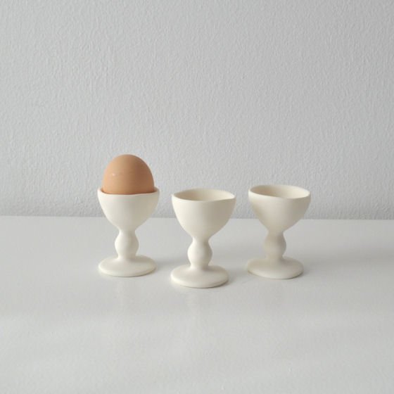 Three white resin egg cups with one egg