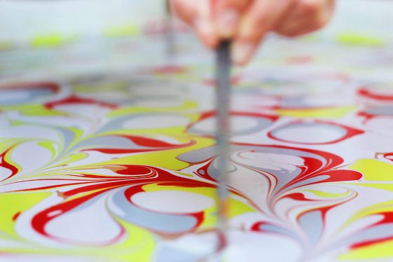 Close up of red, yellow, grey and white marbling inks being swirled on surface of water