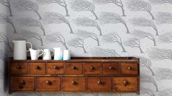 Contemporary wallper with grey trees on white on wall behind chest of drawers