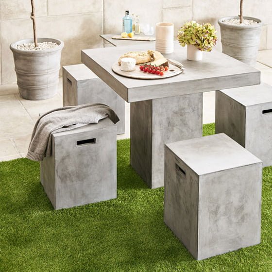 Outdoor grey stone Petra Square Dining Table and Petra Cube stools in garden setting