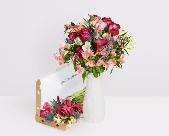 Bloom & Wild Catherine bouquet of pink flowers in white vase next to letterbox pack open with same flowers inside