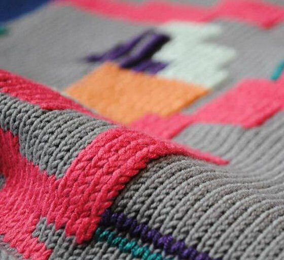 Grey knitted textile with raised pink, orange and white design