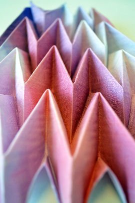Close up photo of zig zag folded fabric in pastel shades of pink, mauve and orange